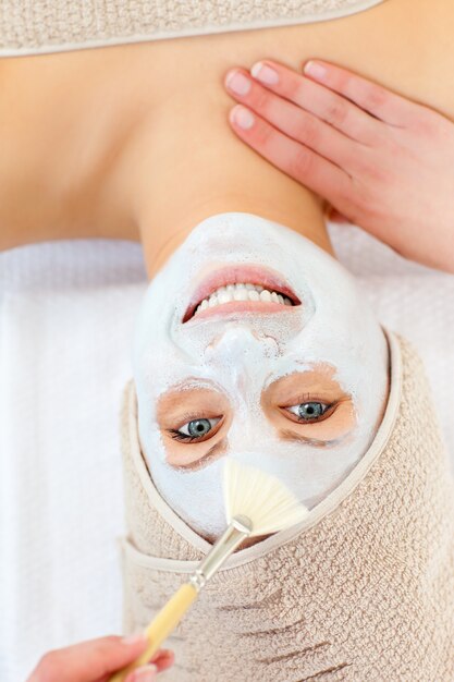 Brillante mujer joven recibiendo crema blanca en su cara