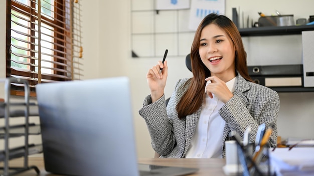 Brillante mujer de negocios asiática trabajando en su proyecto en una laptop en su escritorio de oficina