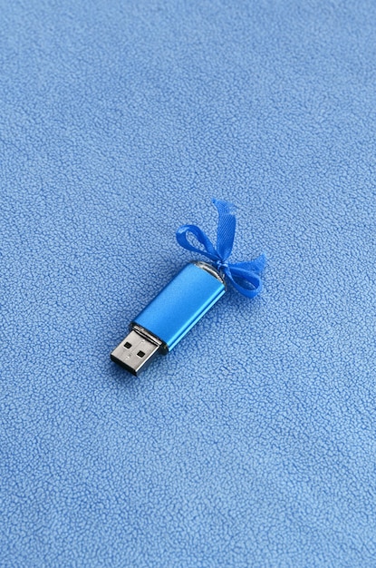 La brillante tarjeta de memoria flash USB azul con un lazo azul se encuentra sobre una manta de suave y peludo tejido de lana azul claro.