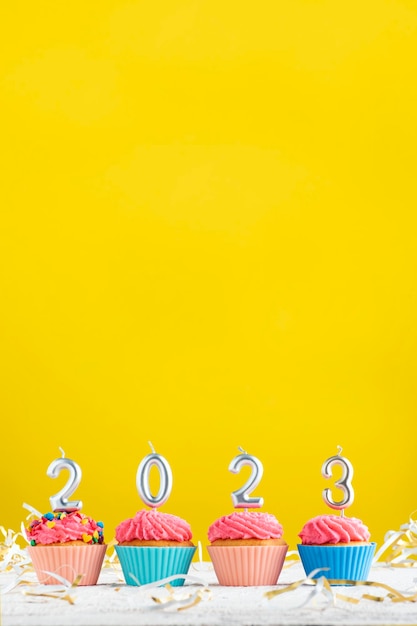Brillante tema navideño con velas en forma de números 2023 en pastelitos sobre fondo amarillo Copiar espacio