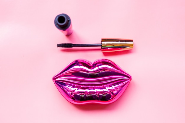 Brillantes labios rosados ​​y máscara sobre fondo rosa brillante, maquillaje y concepto de belleza