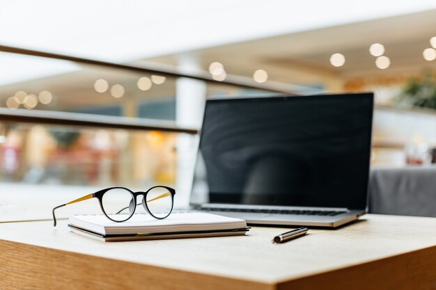 Brille am Arbeitsplatz im Büro in der Nähe von Laptop und Notizblock