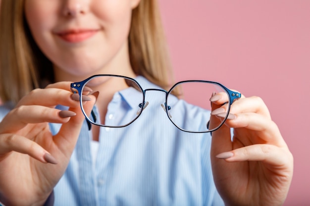 Brille in den Händen. Blaue modische Metallbrille für das Sehen in weiblichen Händen. Augengesundheitsprüfung, Sehkorrektur über Brillen über rosa Farbwand.