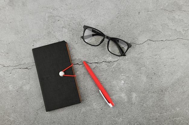 Brille mit Notizbuch auf grauem Hintergrund. Schreibtisch mit Business-Zubehör. Draufsicht