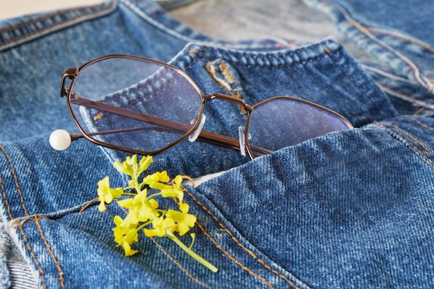 Brillen und gelbe Wildblumen auf der Tasche einer blauen Jeansjacke, Trendbrillen, Retro-Stil