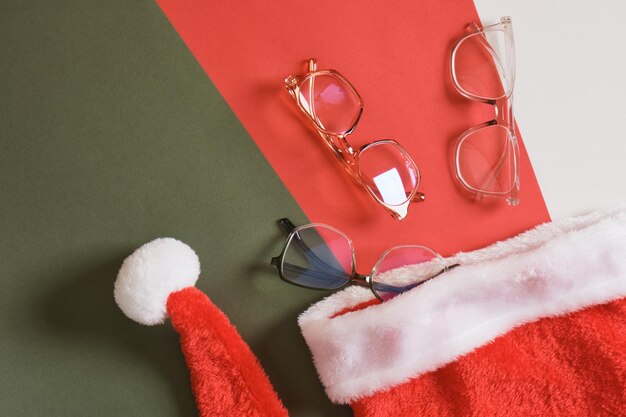 Brillen und Weihnachtsmütze auf rotem und grünem Hintergrund, Optikgeschäft Verkauf vor Weihnachten Kopierraum