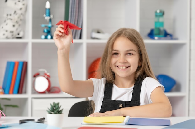 Brincadeira de criança feliz com avião de papel na sala de aula da escola