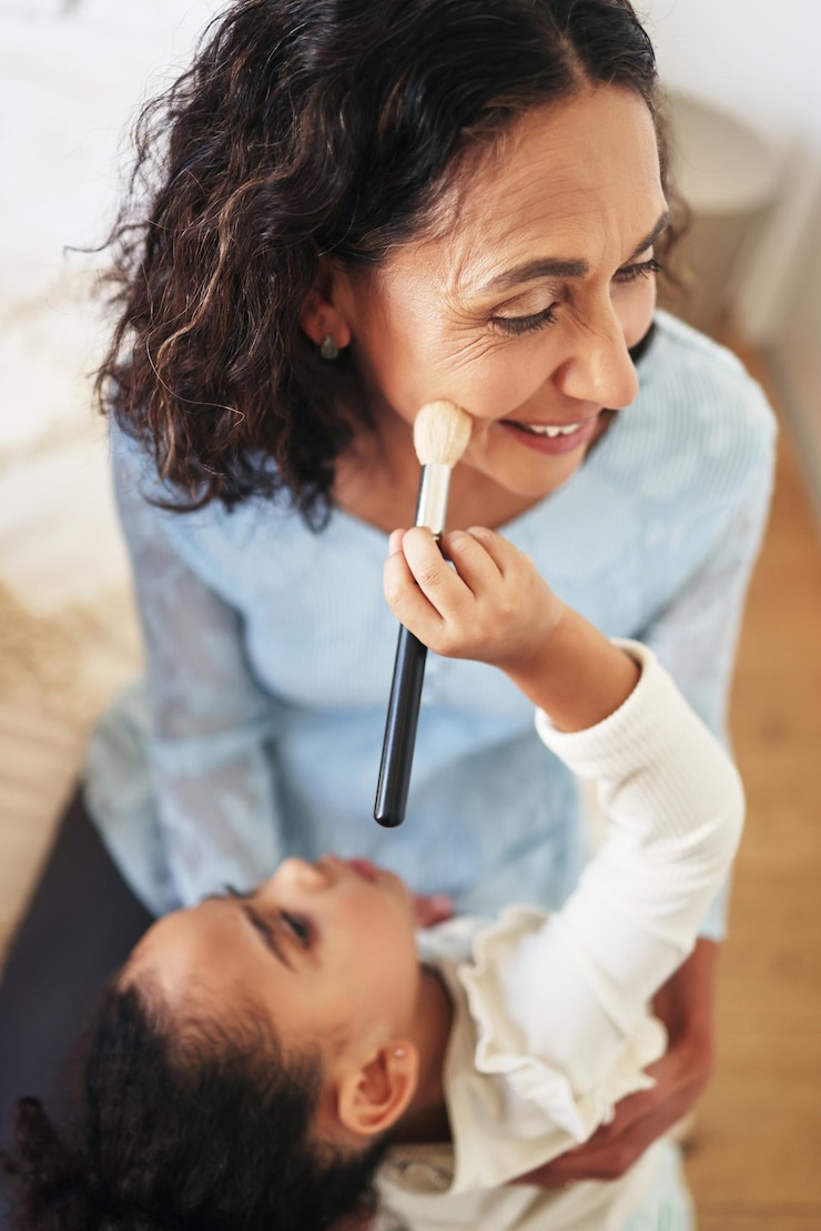 Foto brincalhão feliz e criança fazendo maquiagem de uma avó para diversão e tempo de qualidade sorriso cômico e menina com cosméticos faciais para uma mulher idosa brincando e aplicando blush no rosto