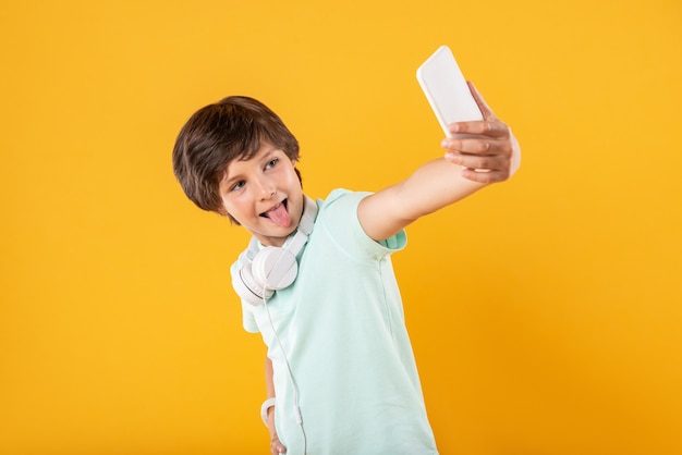 Brincando. Alerta menino magro usando fones de ouvido e tirando selfies