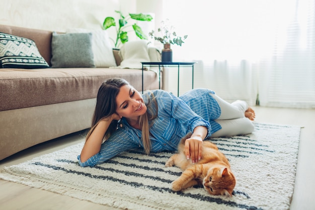 Foto brincando com o gato em casa. jovem mulher deitada no tapete e provocando o animal de estimação.