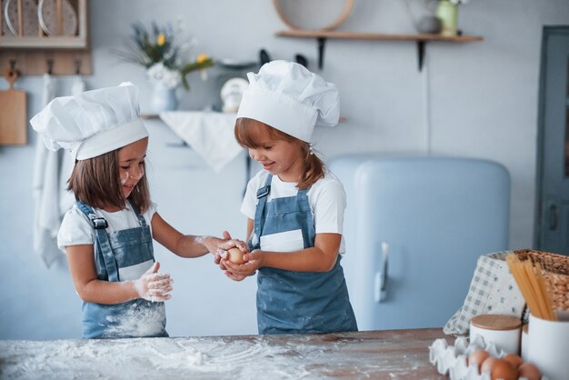 Brincando com ovos. filhos da família com uniforme branco do chef, preparando a comida na cozinha.