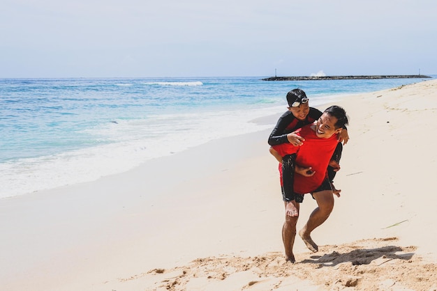 Brincar com a família Pai carregando seu filho nas férias de praia com a família Pai e filho jogo