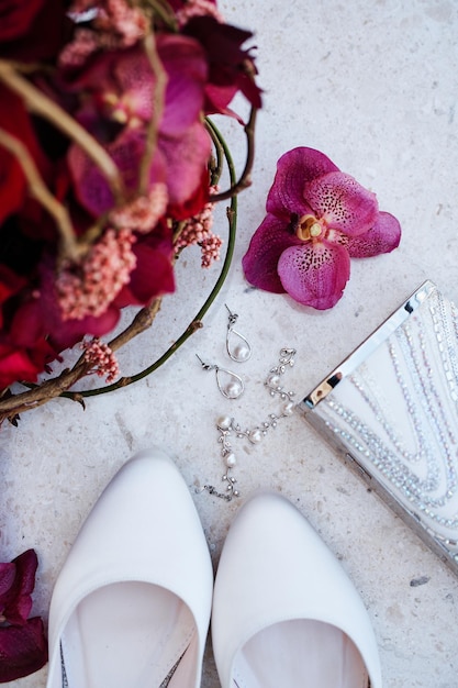 Foto brincos de pérola, uma pulseira e sapatos deitam-se ao lado de um buquê de flores em uma mesa de granito