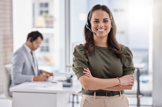 Brindando un excelente servicio al cliente Retrato de una joven agente del centro de llamadas de pie con los brazos cruzados en una oficina con su colega en el fondo