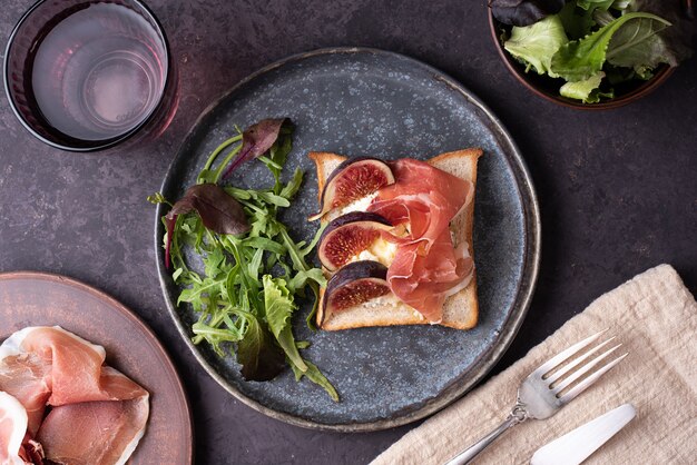 Brindis con jamón e higos, crostini con jamón italiano y ricotta, snack sobre un fondo oscuro, primer plano.