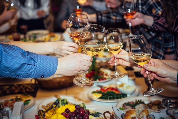 Brindis en la mesa festiva. Manos sosteniendo vasos con bebidas alcohólicas, primer plano. Familiares y amigos tintineando copas.