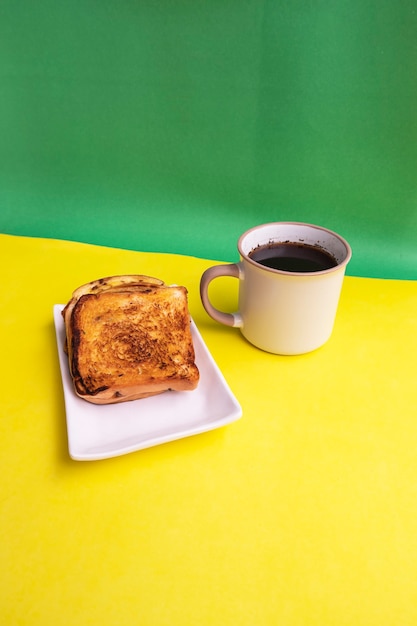 Brindis En Plato Blanco Y Taza De Café Negro Sobre Fondo De Papel Amarillo Y Verde. Tostadas Y Café Negro Para El Desayuno. Foto vertical