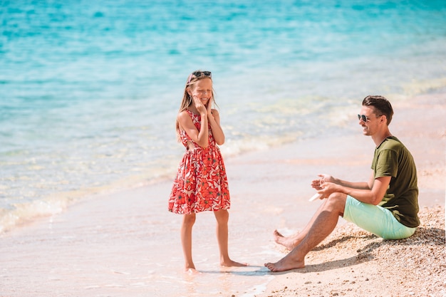 Bringen Sie das Auftragen der Sonnenschutzcreme an seiner Tochter am tropischen Strand hervor