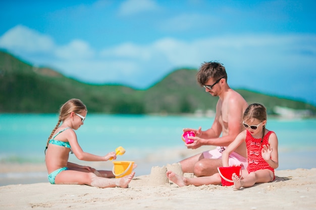 Bringen Sie und zwei Mädchen hervor, die mit Sand auf tropischem Strand spielen