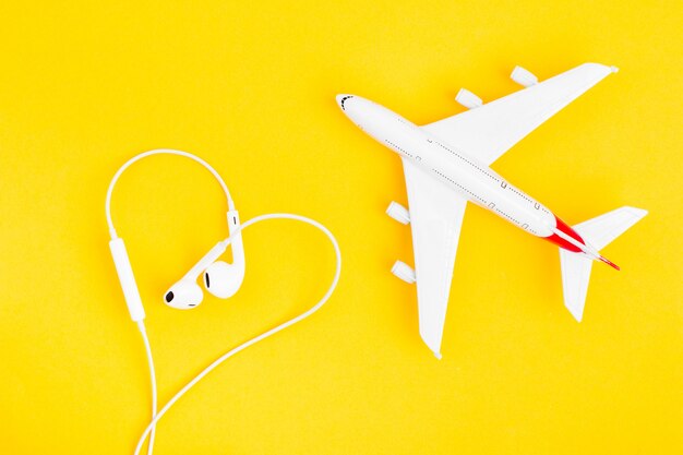 Brinque o avião e os fones de ouvido em forma de coração em fundo amarelo.