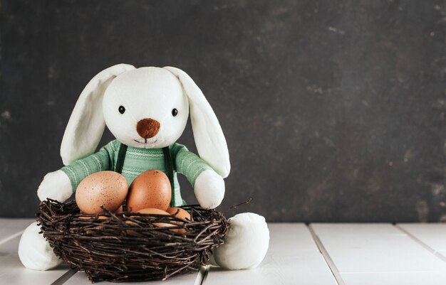 Brinque o ninho de coelho e vime com ovos de galinha em um fundo cinza escuro. Espaço de cópia de Páscoa.