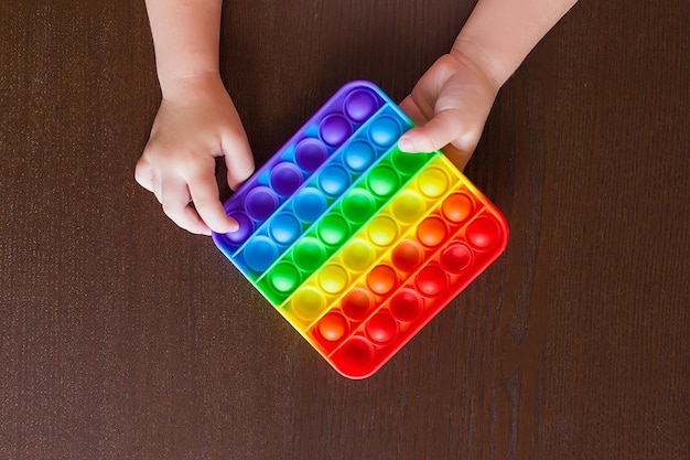 Brinquedo anti-stress sensorial infantil com covinhas em uma mesa preta popit quadrado de um tom de arco-íris de cor brilhante a tendência do brinquedo de silicone de vista superior de 2021