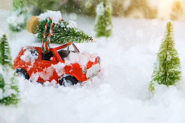 Brinquedo de carro vintage vermelho transportando uma árvore de Natal para casa através de uma terra maravilhosa de inverno nevado. Profundidade de campo rasa extrema com foco seletivo no veículo