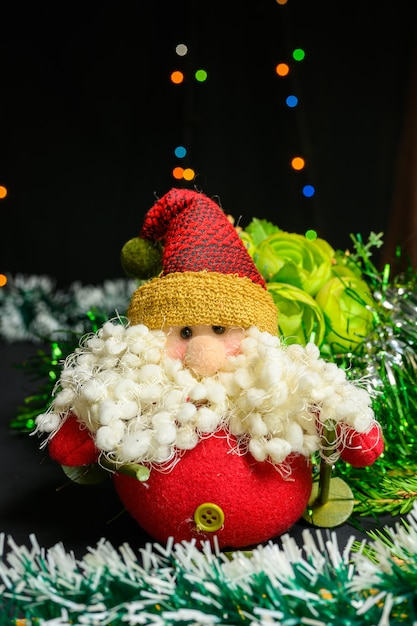 Brinquedo de Papai Noel com uma barba grande no fundo de uma guirlanda e flores. Conceito de Natal e ano novo em fundo preto.