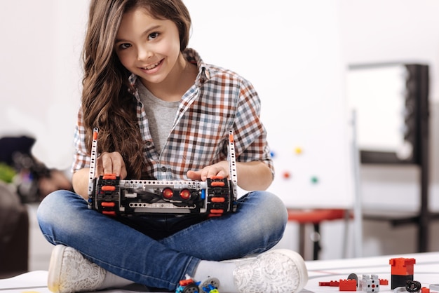 Brinquedo digital de programação. menina talentosa e habilidosa encantada sentada no laboratório de robótica segurando um robô digital enquanto o programa