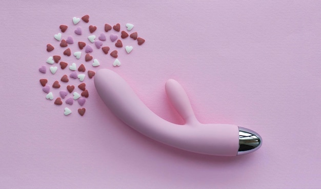 Brinquedo vibrador rosa para adultos encontra-se em um fundo rosa ao lado de corações decorativos imitando um orgasmo foto conceitual