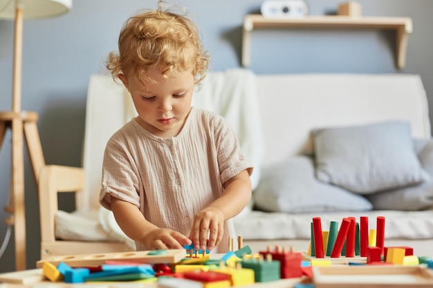 Brinquedos de aprendizagem coloridos Blocos de construção divertidos Atividades lúdicas de creche Jogos de desenvolvimento infantil Garotinha loira brincando com brinquedos de classificação de madeira no interior de casa