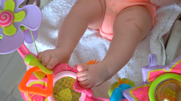 Brinquedos de carrinho de bebê recém-nascido. Pernas de bebê infantil e brinquedos de chocalho coloridos. Atividade inicial de bebês.