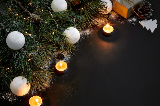 Brinquedos de natal queimando velas e galho de abeto em fundo preto, vista superior, espaço para texto