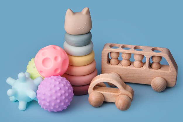 Brinquedos educativos coloridos das crianças montessori sobre um fundo azul. Bolas sensoriais para crianças, carros de madeira e pirâmide de silicone, conjunto multi-bolas de plástico texturizado para bebês e crianças pequenas, brinquedo torre.