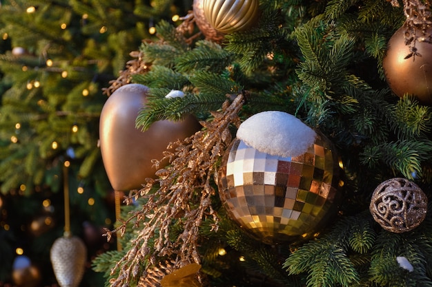 Brinquedos em uma árvore de Natal na neve, neve em uma bola de natal dourada