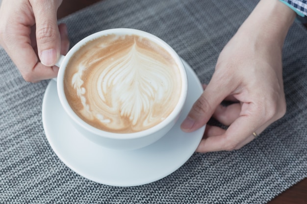 Brita hält eine weiße Kaffeetasse mit einem Latte Art Muster.