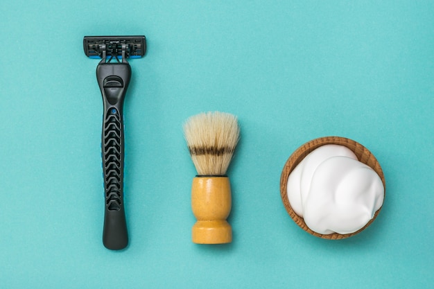 Foto brocha de afeitar, navaja y espuma de afeitar sobre un fondo azul. preparado para el cuidado de la cara de un hombre. endecha plana.