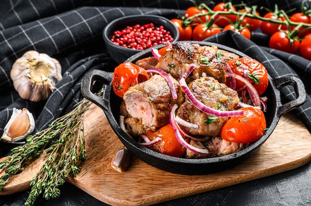 Brocheta de cerdo con cebolla y tomate en sartén. Carne a la parrilla. Fondo negro. Vista superior.