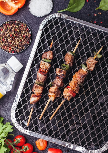 Brocheta de cerdo a la parrilla con pimentón en parrilla de barbacoa de carbón desechable con verduras frescas en negro