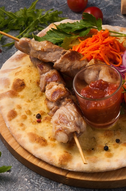 Brocheta de cerdo sobre pan de pita con verduras y salsa de tomate. Marco vertical