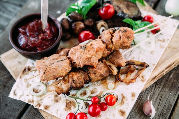 Foto brocheta de cerdo con verduras y salsa de tomate closeup sobre una mesa de madera