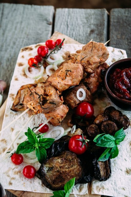 Foto brocheta de cerdo con verduras y salsa de tomate closeup sobre una mesa de madera