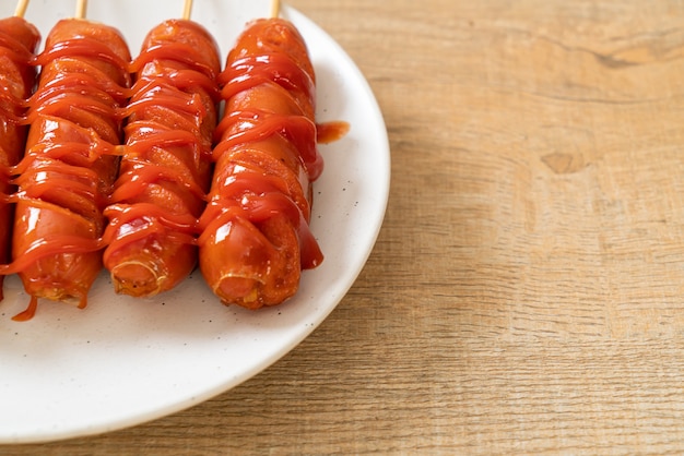 Brocheta de salchicha frita con salsa de tomate en la placa blanca.