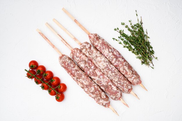 Brochetas de carne cruda de res y cordero, salchichas con ingredientes a la parrilla sobre fondo de mesa de piedra blanca, vista superior, endecha plana