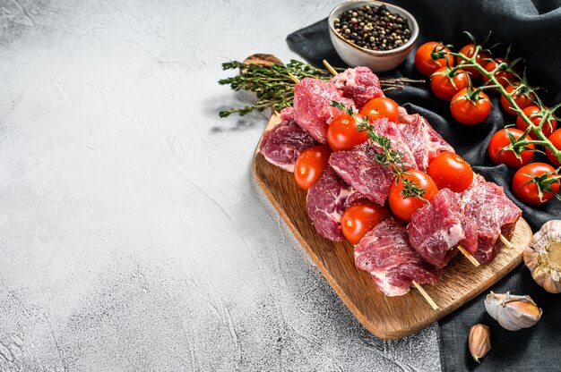 Brochetas de carne cruda en tabla de cortar.