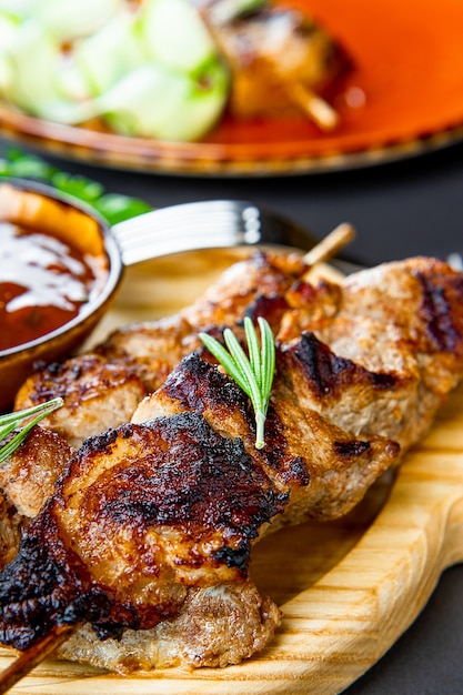 Brochetas de cerdo a la parrilla con ensalada de pepino y salsa barbacoa en la tabla de cortar de cerca vertical