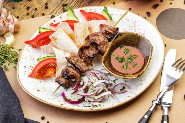 Brochetas de cerdo en un plato con salsa en una mesa de madera