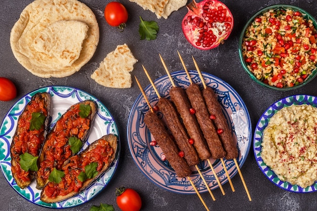 Brochetas clásicas, ensalada tabulé, baba ganush y berenjena al horno con salsa. Plato tradicional de oriente medio o árabe. Vista superior.