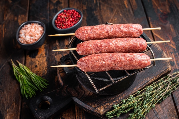 Brochetas crudas de kofta o lula kebabs en una parrilla con hierbas. Fondo de madera oscura. Vista superior.