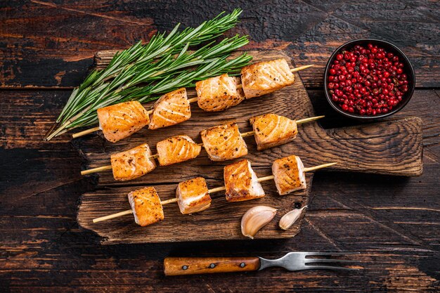 Brochetas de kebab de pescado salmón a la plancha sobre tabla de madera. Fondo de madera oscura. Vista superior.